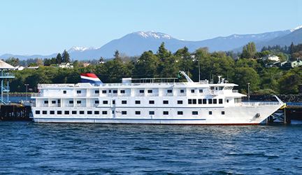 The American Spirit small cruise ship docked in San Juan Islands with tall mountains in the distance.