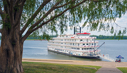 American Heritage, an American Cruise Lines Paddlewheeler decorated with patriotic red white and blue bunting flags on the front railings, docked along the Mississippi River in Paducah, KY letting passengers off from the front of the ship.