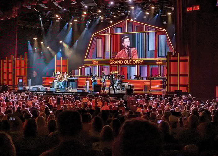 A live concert at the Grand Ole Opry in Nashville, where a male singer and his band performs in front of a large crowd of hundreds of people.