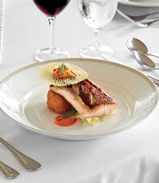 A salmon dish accompanied by a wine glass and a glass of water, served on American Cruise Lines.