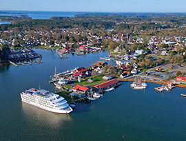 An aerial view of an American Cruise Lines small cruise ship docked in St. Michaels along the Chesapeake Bay with trees and buildings filling the shore.