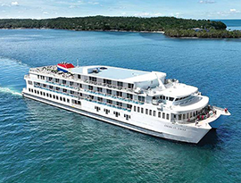 American Eagle Coastal Cat, a small white cruise ship sailing along the bright blue Gulf Coast waters in Jacksonville with thick forest land in the distance.