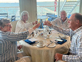 Two couples sit together at a round dinner table on an American Riverboat having a toast with their champagne glasses before a meal served by American Cruise Lines.