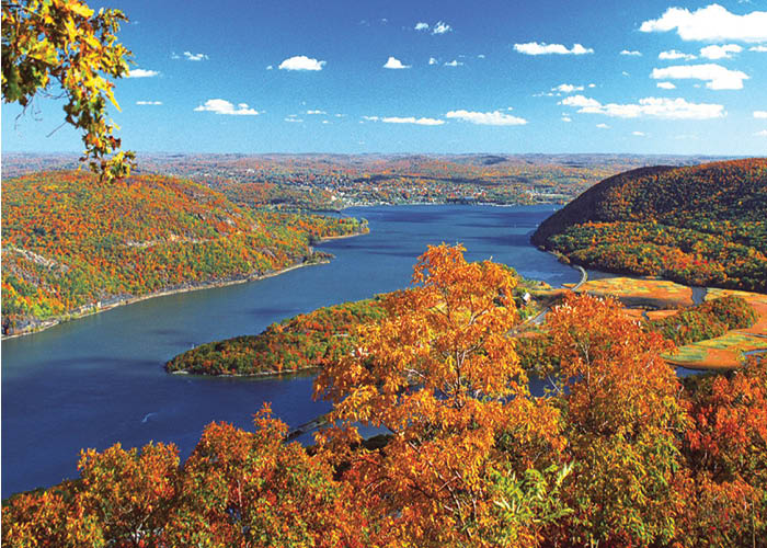 An aerial view of the Hudson River with cliffs covered in autumn leaves on each side of the water, and small mountains in the distance.