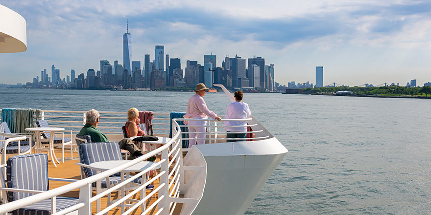 American Cruise Lines guests standing and sitting on the sun deck aboard a Coastal Cat with views of the New York City skyscrapers in the distance.