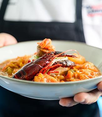 A close up view of a person holding a bowl of Crawfish Etouffee served on American Cruise Lines.