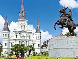 The St. Louis Cathedral with three dark grey spires stands in Jackson Square in New Orleans, while a statue of a rider on a horse is off to the right.