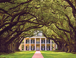 A historic plantation in Louisiana, Houmas House Plantation has two story pillars on all sides, grand porches and is set amongst beautiful grounds and gardens with a red brick pathway. 