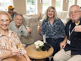 A group of cruise guests holding up glasses of champagne while sitting in the Chesapeake Lounge aboard a Coastal Cat. There are a few sofas in the background with people sitting on them.