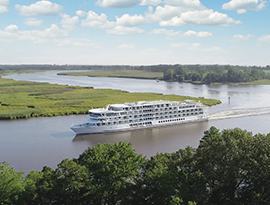 An American riverboat gliding along the Mississippi River, surrounded by green landscapes, under a blue sky with a few clouds.