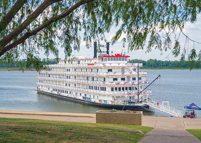 American Heritage, an American Cruise Lines Paddlewheeler decorated with patriotic red white and blue bunting flags on the front railings, docked along the Mississippi River in Paducah, KY letting passengers off from the front of the ship.