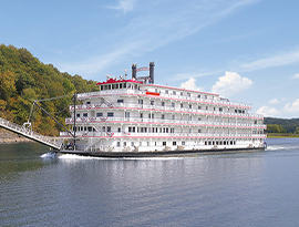 American Heritage paddlewheeler gliding along the Mississippi River. The white cruise ship has is decorated with patriotic red white and blue bunting flags on the front of every railing.