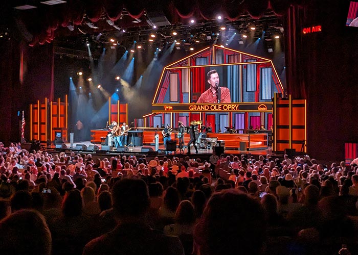 A live concert at the Grand Ole Opry in Nashville, where a male singer and his band performs in front of a large crowd of hundreds of people.