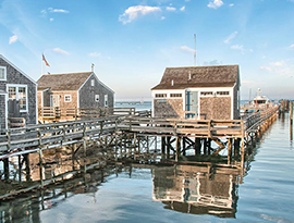 Beach cottages with blue doors on the water supported and connected by a wooden bridge in Nantucket Island.