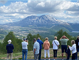 A group of American Cruise Lines guests viewing  and photographing Mount St. Helens, tall mountains that are partially covered in snow.