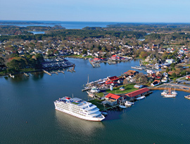 An aerial view of an American Cruise Lines small cruise ship docked in St. Michaels along the Chesapeake Bay with trees and buildings filling the shore.