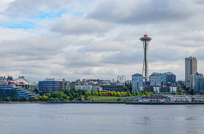 The Seattle cityscape featuring tall skyscrapers, the Seattle Space Needle, and the Seattle Great Wheel, a large Ferris wheel at the edge of Pier 57.