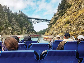 American Cruise Lines guests on a jet boat ride through Deception Pass State Park, with bright blue water ahead of the boat and cliffs on each side with a bridge connecting them in the middle.