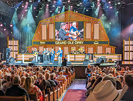 A live concert at the Grand Ole Opry in Nashville, where a band performing with instruments like guitars and violins in front of a large crowd of people.