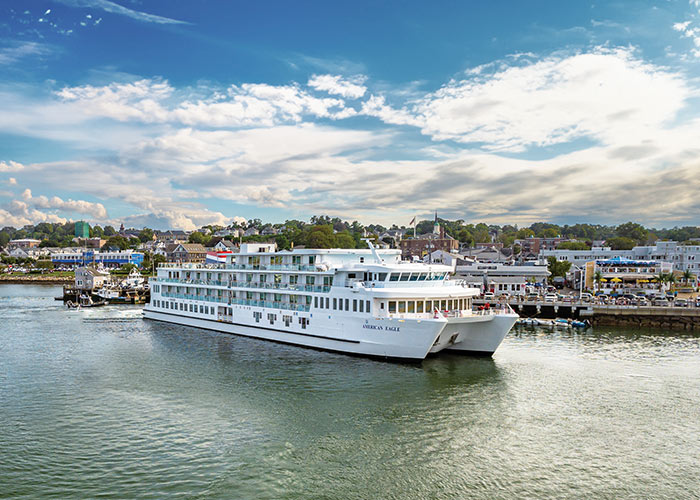 American Eagle Coastal Cat small cruise ship docked along the calm waters in Plymouth, with the towns buildings and nature in the near distance.