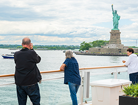 Passengers on the sun deck of an American Cruise Lines small cruise ship observing the green colored Statue of Liberty, close enough to see the details of the statue. 