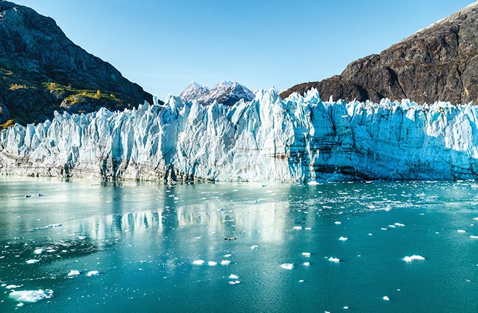 A crisp white glacier above the surface of the blue, icy waters of Glacier Bay Basin under a bright blue sky.