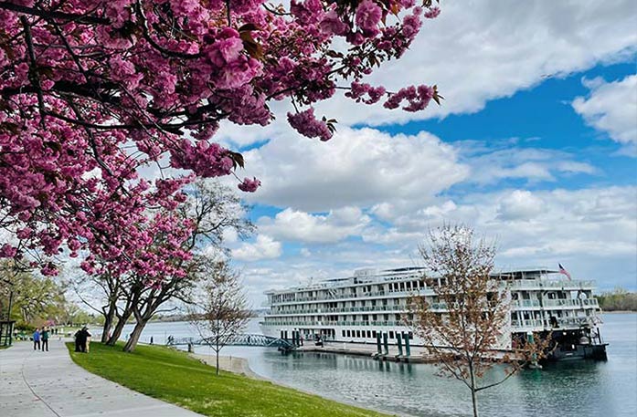 An American Riverboat docked along the Columbia River in Richland, with a small bridge over the water, connecting cruise passengers to the sidewalk.