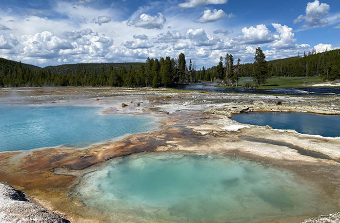 Three circular hot springs with a small amount of steam coming off of the various blue-colored water, surrounded by the forests in Yellowstone National Park.