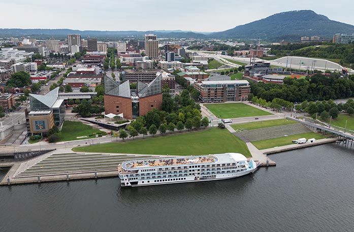 The American Riverboat American Serenade docked along the Tennessee River with views of Chattanooga's Tennessee Aquarium and cityscape in the background. 