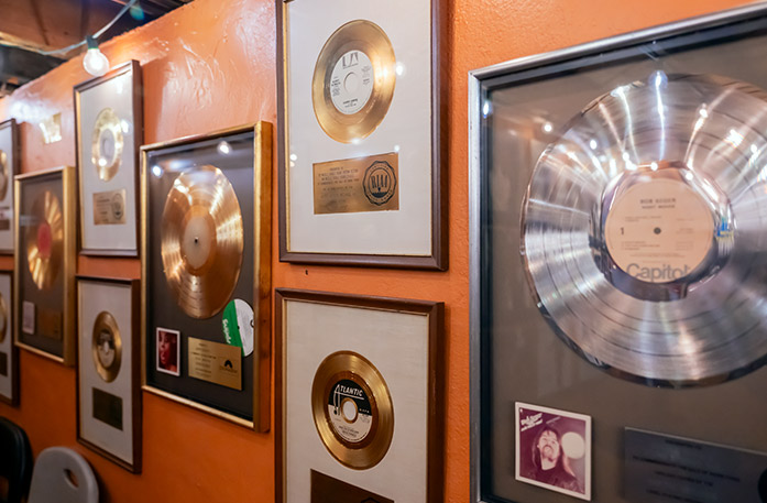 An orange wall inside of Fame Recording Studios in Florence with several gold records and one silver record in frames hung on it.