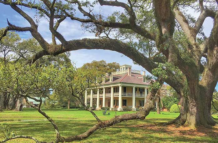 A historic plantation in Louisiana, Houmas House Plantation has two story pillars on all sides, grand porches and is set amongst beautiful grounds and gardens with a red brick pathway. 