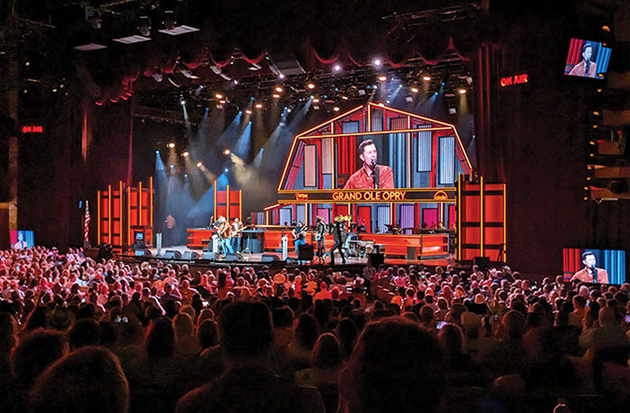 A live concert at the Grand Ole Opry in Nashville, where a male singer and his band performs in front of a large crowd of hundreds of people.