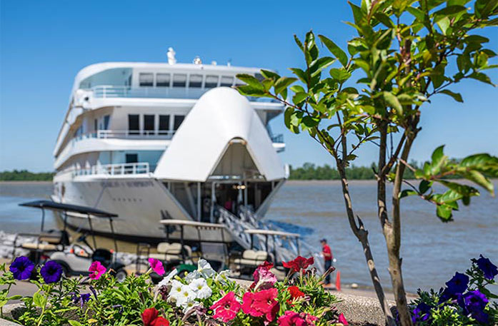 Colorful flowers line the shore with the American Riverboat American Symphony docked in Paducah in the background, with its Retractable Bow Gangway lifted for a ramp to connect it to shore.