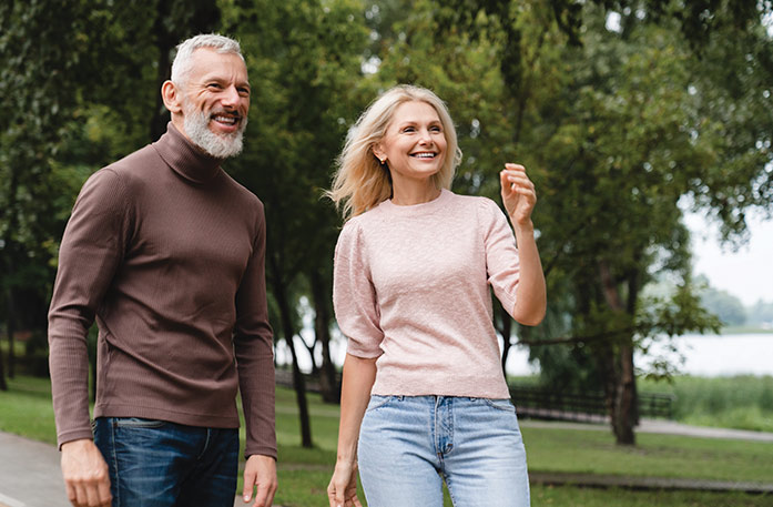 A man with a white beard and woman with blonde hair are smiling while walking through a park in Bristol.