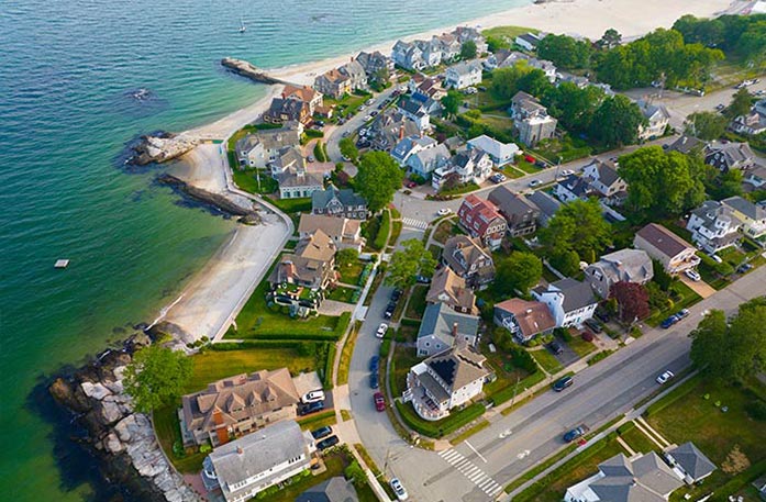 A birds-eye-view of the New London shoreline, with a view of a neighborhood with several houses along the blue-green water of Long Island Sound.