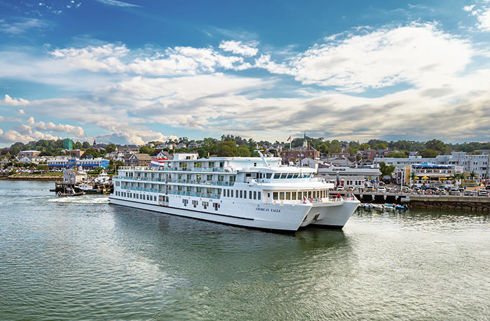 American Eagle Coastal Cat docked along the calm waters in Plymouth, with the towns buildings and nature in the near distance.