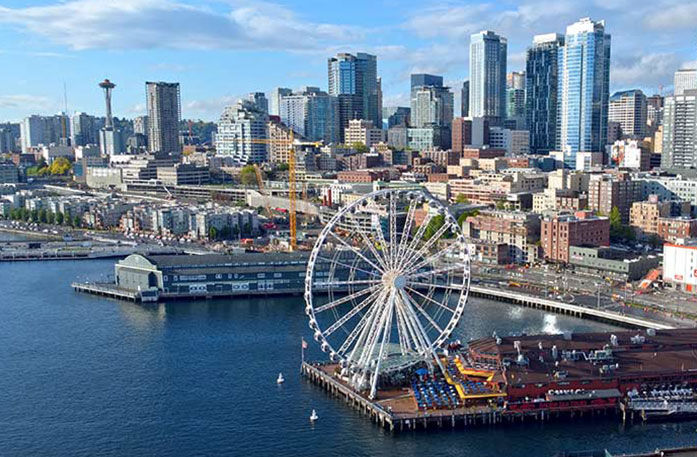 The Seattle cityscape featuring tall skyscrapers, the Seattle Space Needle, and the Seattle Great Wheel, a large Ferris wheel at the edge of Pier 57.