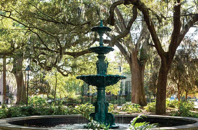 Semi-Quincentenary Fountain, a tall, dark green fountain located in Lafayette Square in Savannah surrounded by Live Oak Trees with Spanish moss hanging down.