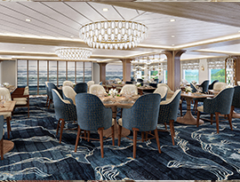 The restaurant on American Anthem, where there are several round tables and navy blue chairs along the blue and white patterned carpet, and two round chandeliers hanging from the ceiling. There are large windows with clear views of the Columbia River on one wall, and floor-to-ceiling paintings on the back wall.