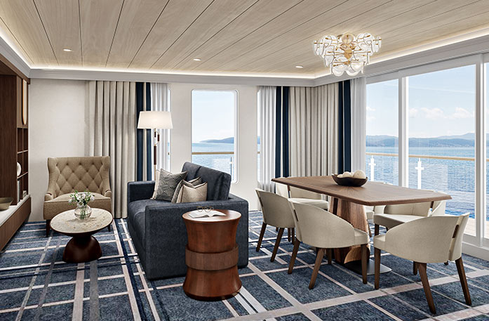 The spacious Signature Suite on American Encore, with floor-to-ceiling glass windows along the back wall overlooking the private balcony and the Columbia River. There is a wooden dining table with six tan chairs around it, a navy blue sofa, a tan armchair, and a round coffee table.
