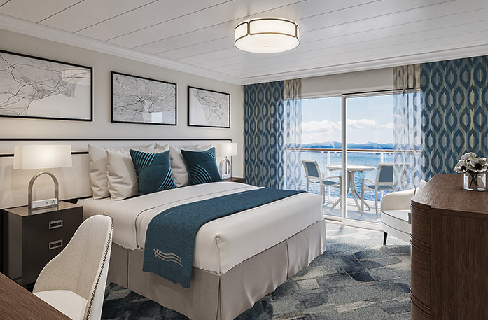 The Vista Balcony stateroom on American Encore,  with large floor-to-ceiling sliding glass doors, with blue curtains on each end, that lead to a private balcony with a table and chairs overlooking the Columbia River, a bed with white bedding and two blue pillows, and three white paintings with blue lines above the bed. There is an end table with a lamp on each side of the bed. 