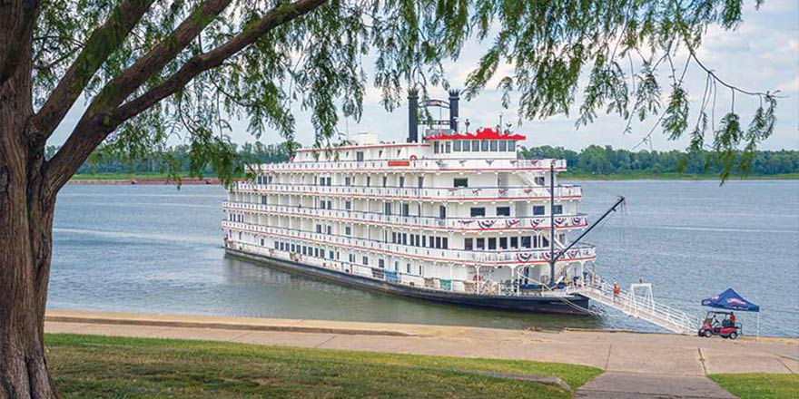 American Heritage, an American Cruise Lines Paddlewheeler decorated with patriotic red white and blue bunting flags on the front railings, docked along the Mississippi River in Paducah, KY letting passengers off from the front of the ship.