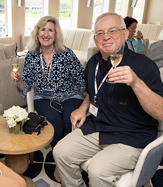 A man and woman smiling while each holding a glass of champagne, sitting around a small table in a lounge aboard an American Cruise Lines small ship.